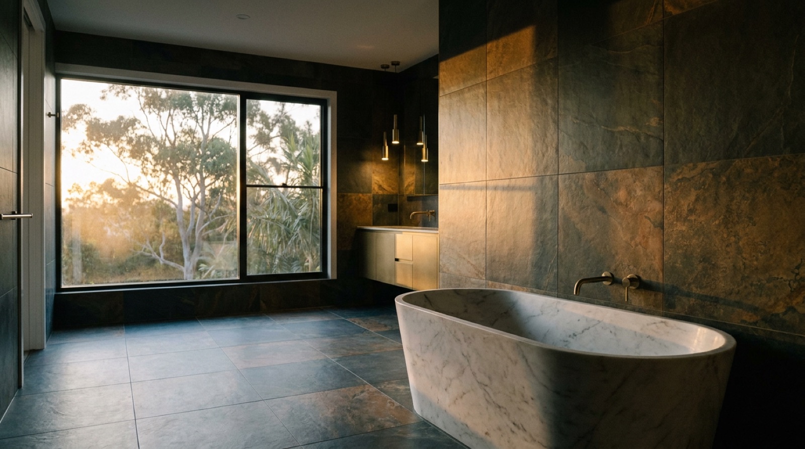 A tiled bathroom with a freestanding bath beside a large window at dusk