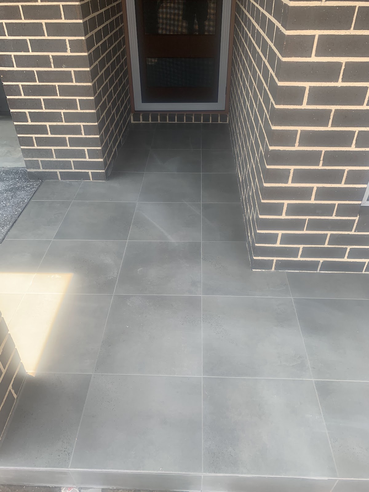 An outdoor entry with large-format tiles laid between brick columns