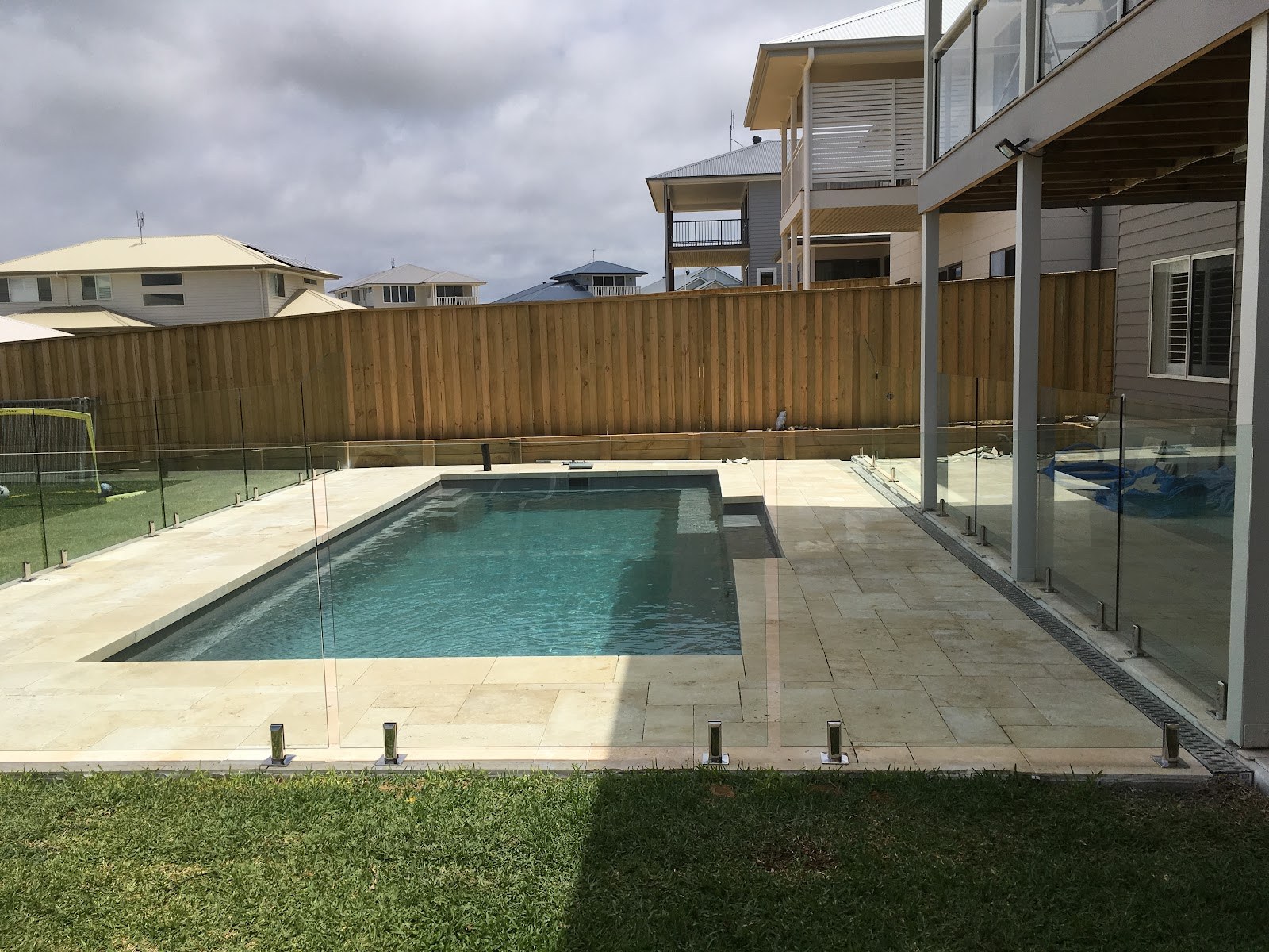 A backyard swimming pool with a tiled surround and glass fence, tiled by Clear Cut Tiling