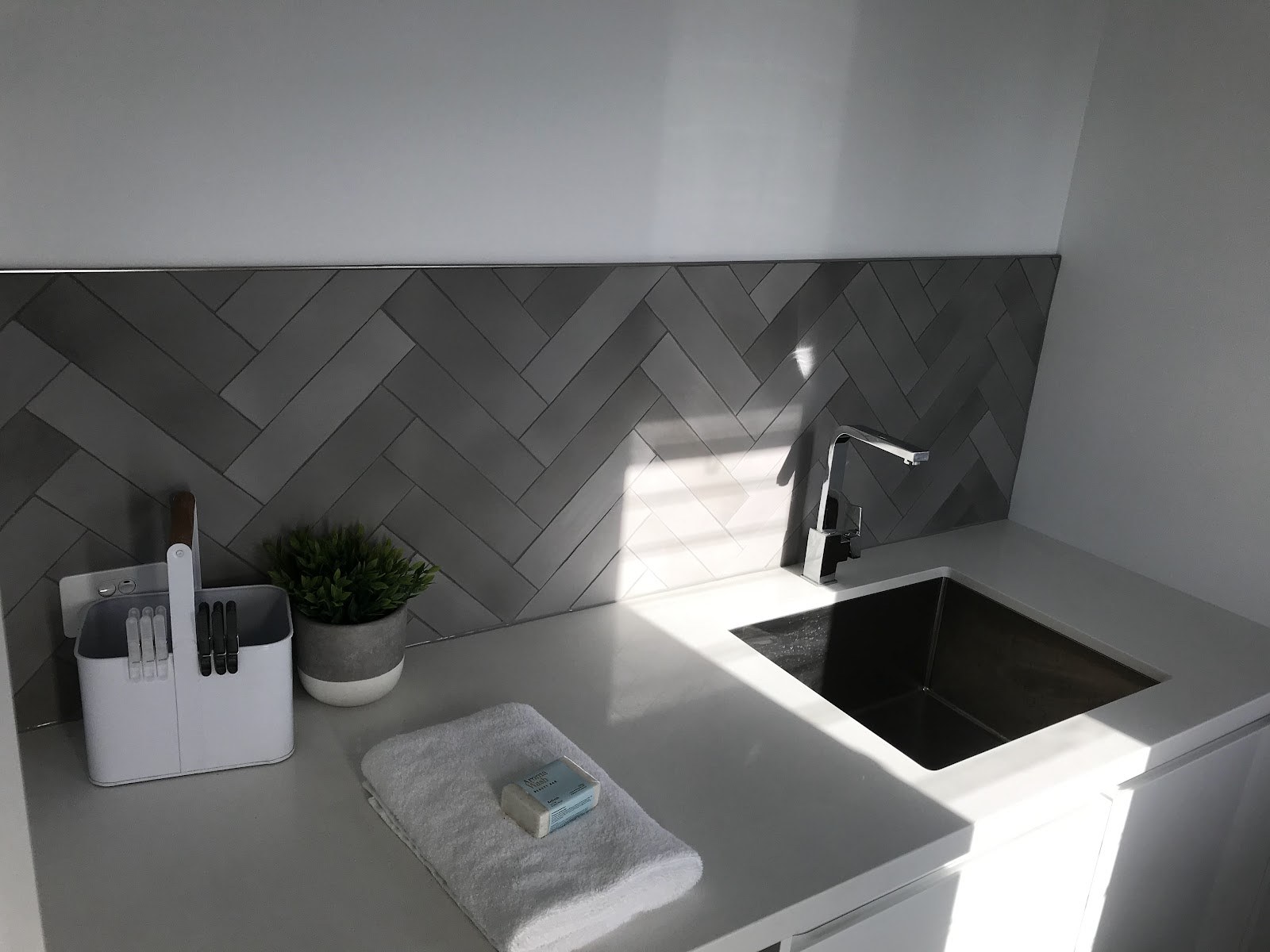 A grey herringbone splashback tiled behind a kitchen sink