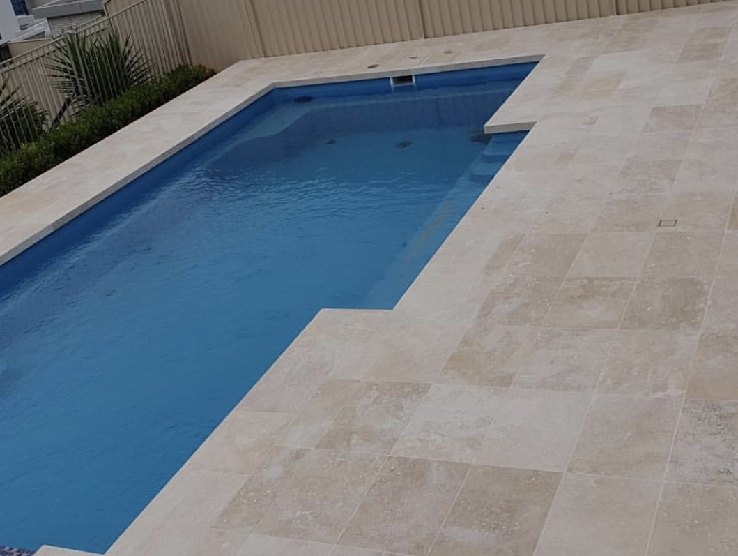 A swimming pool with a stone-tiled surround laid by Clear Cut Tiling