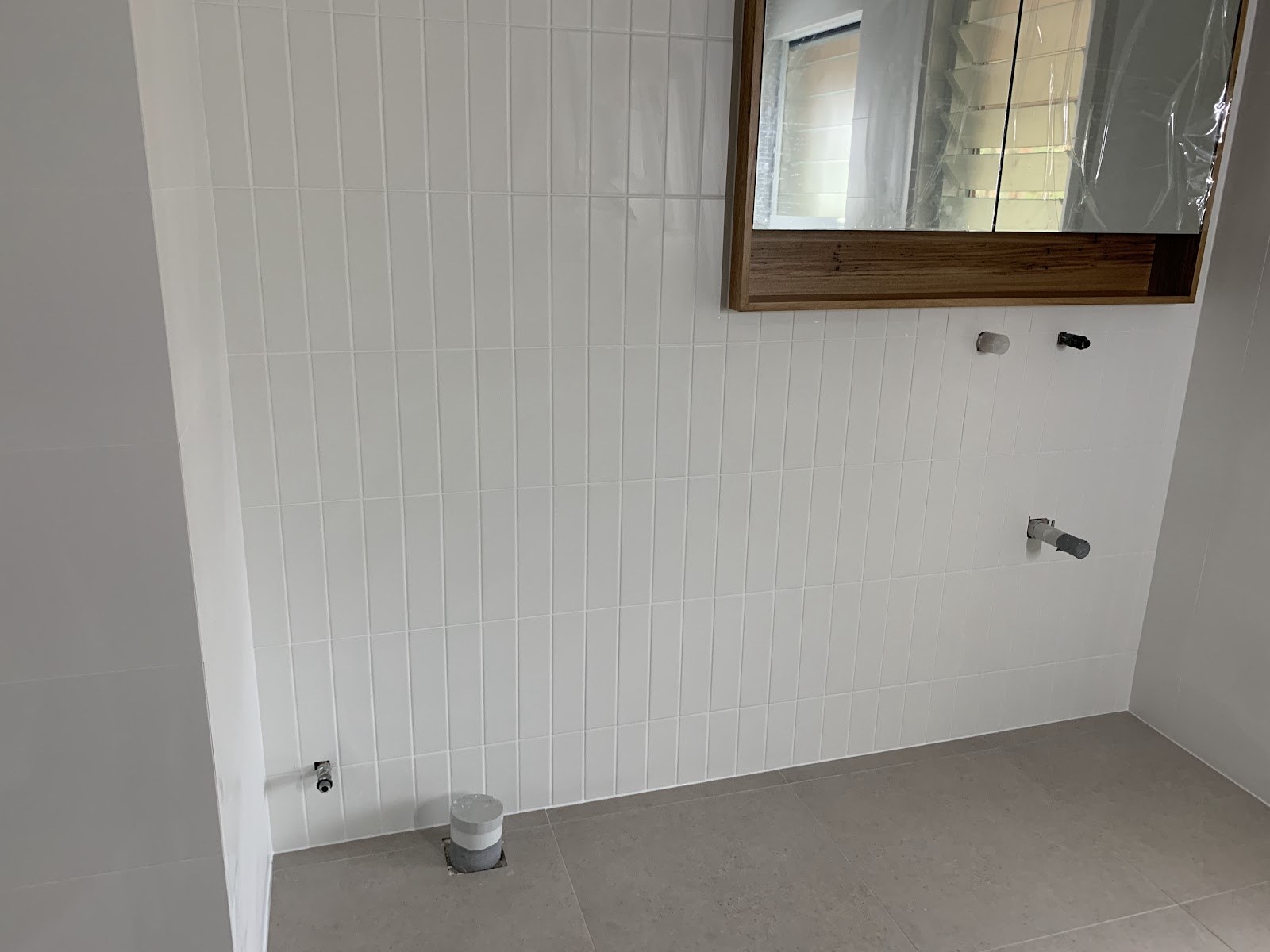A white tiled wall beside a timber-framed window, tiled by Clear Cut Tiling